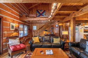 A cozy cabin interior with a wooden interior, a black leather sofa, a red cushioned chair, and a wooden coffee table. - Daniel Boone Lodge (Boone)