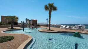 A pool area with clear water, palm trees, lounge chairs, and a view of the ocean. - Laketown Wharf 809 (Panama City Beach)