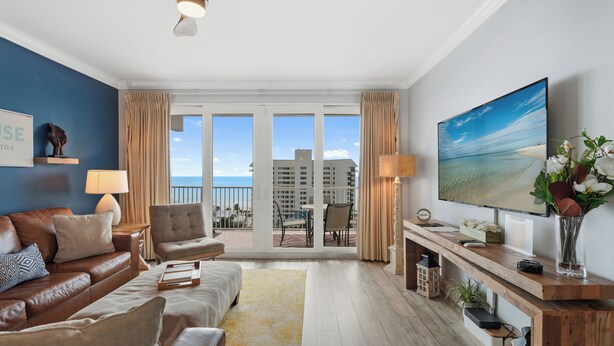 A modern living room with a leather sofa, a flat-screen TV, and a balcony with a view of the ocean. - Laketown Wharf 809 (Panama City Beach)