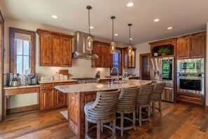 A modern kitchen with wooden cabinets, a large island with bar stools, stainless steel appliances, and pendant lighting. - One Sweet Getaway at Eagles Nest (Banner Elk)