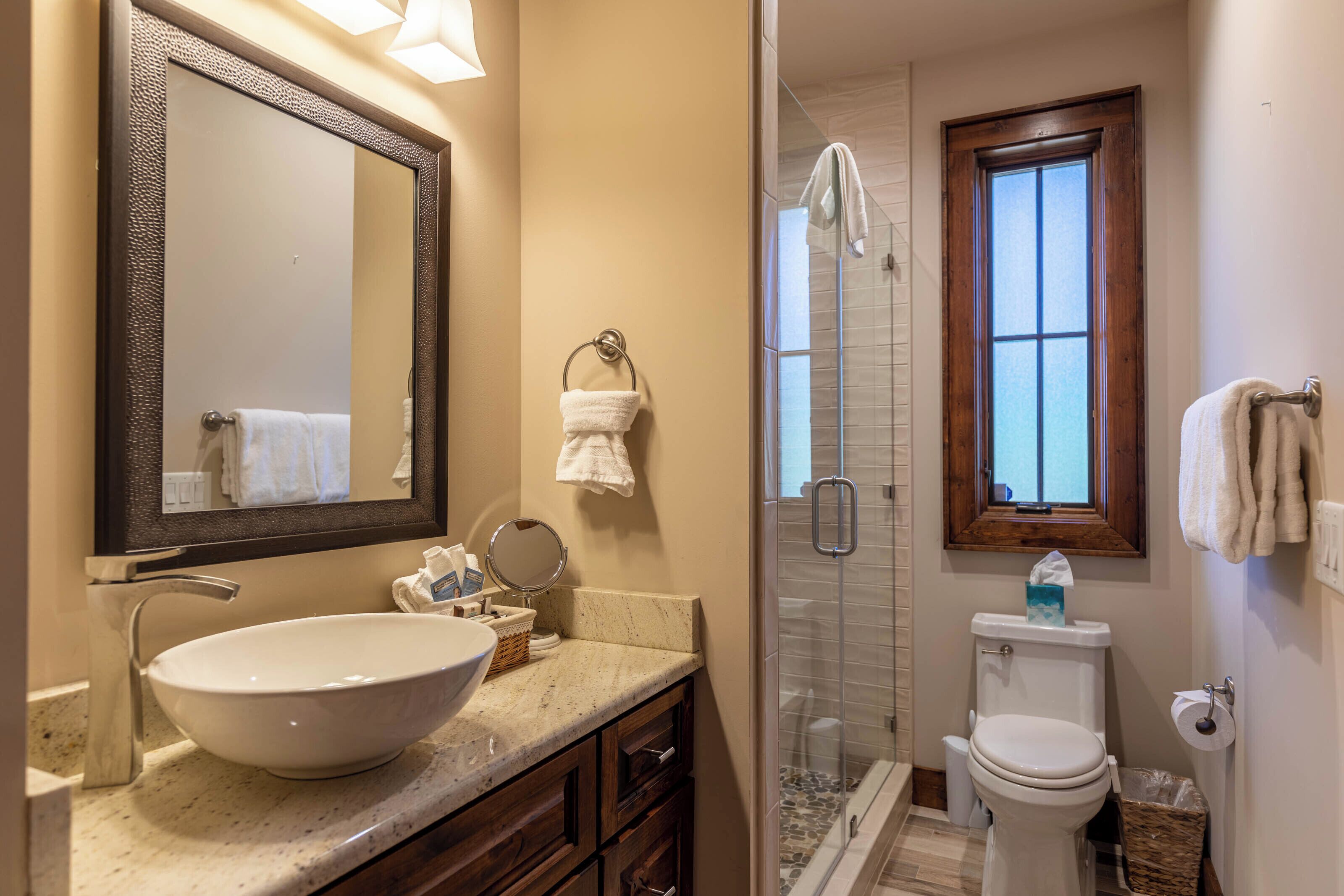 Un bagno con un ampio specchio, un lavabo sospeso, una doccia vetrata e un water.