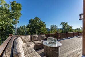 A wooden deck with a wicker sofa and a glass-top table, surrounded by a wooden railing. - One Sweet Getaway at Eagles Nest (Banner Elk)