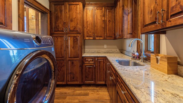 Una cocina con armarios de madera, lavadora integrada, encimeras de granito y un lavamanos.