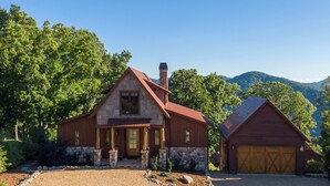 Una casa de piedra de dos pisos con techo rojo, chimenea y garaje.