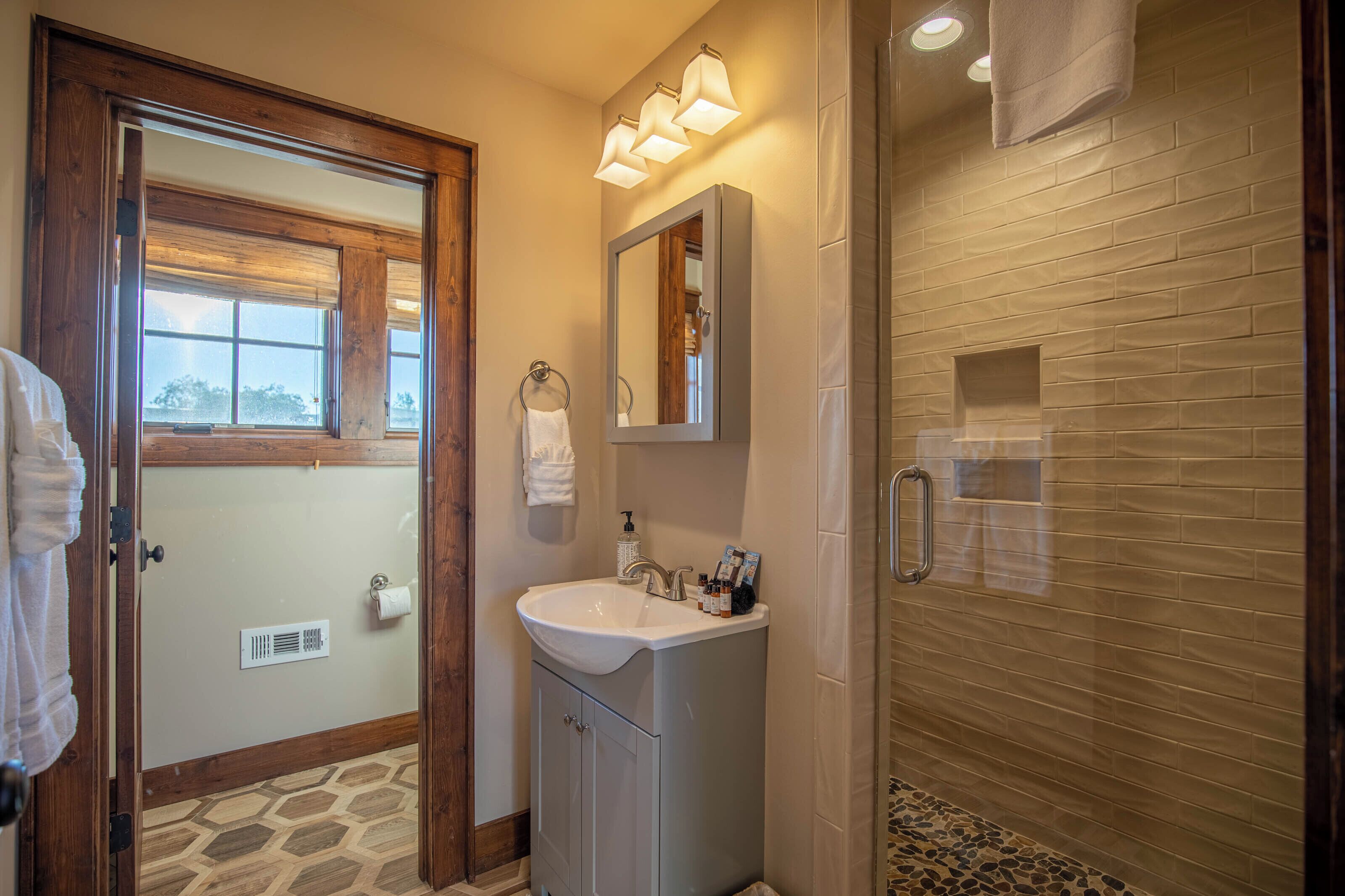A bathroom with a wooden door, a sink with a mirror, and a shower area.