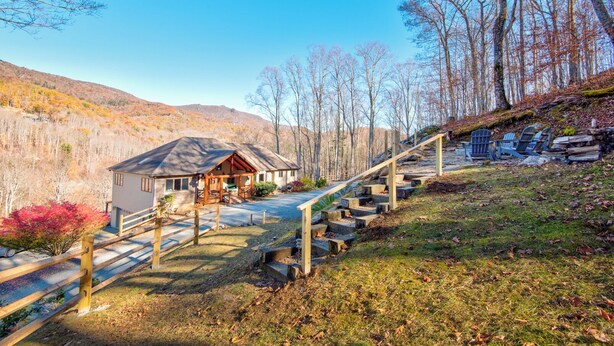 A cabin with a porch, a staircase, and a view of the surrounding forest. - Boulder Sky at River Run (Banner Elk)
