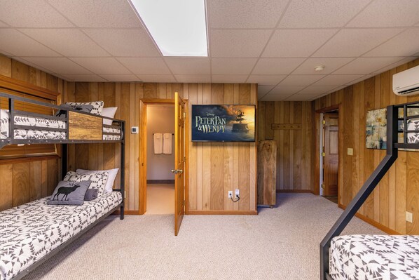 A room with bunk beds, a wooden wall, a poster of 'Peter Pan & Wendy', and a door leading to another room.