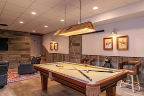 Une table de billard dans une pièce dotée d’un plafond en bois, d’un tapis et de deux tableaux encadrés accrochés au mur.