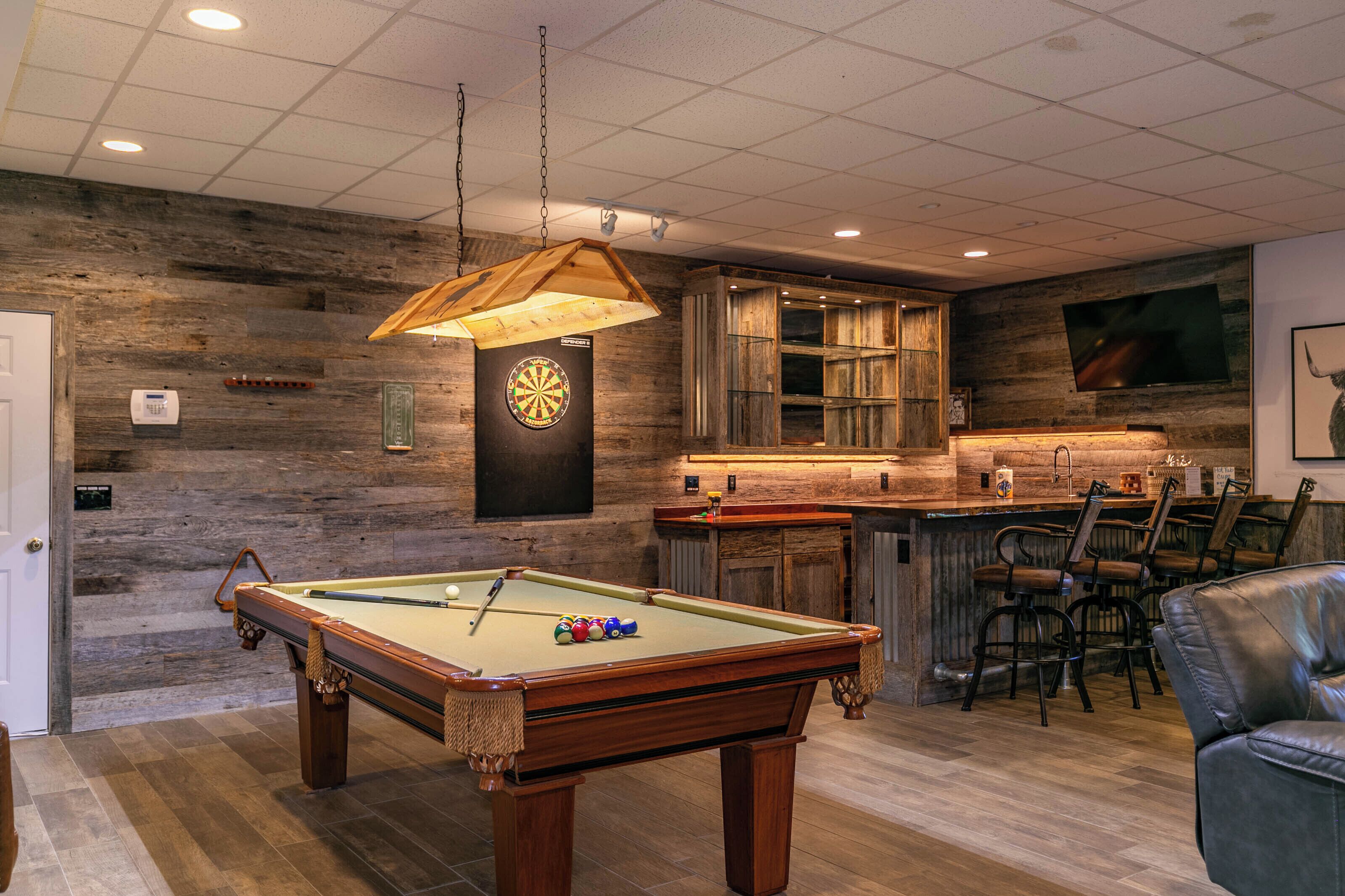 A pool table with balls, a dartboard, and a bar area with chairs.