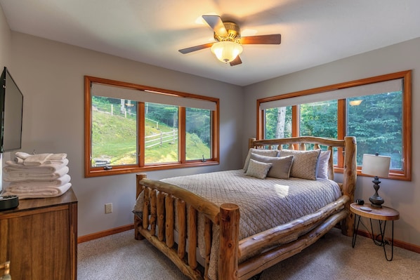 Une chambre à coucher avec un lit en bois, de grandes fenêtres, un ventilateur de plafond et une table de chevet avec une lampe.