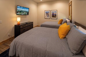 Ein Schlafzimmer mit zwei Betten, einem an der Wand befestigten Fernseher und zwei gerahmten Postern.