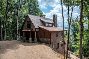 Ein rustikales Blockhaus mit Steinkamin, Holzfassade und einem Schotterweg, umgeben von hohen Bäumen.