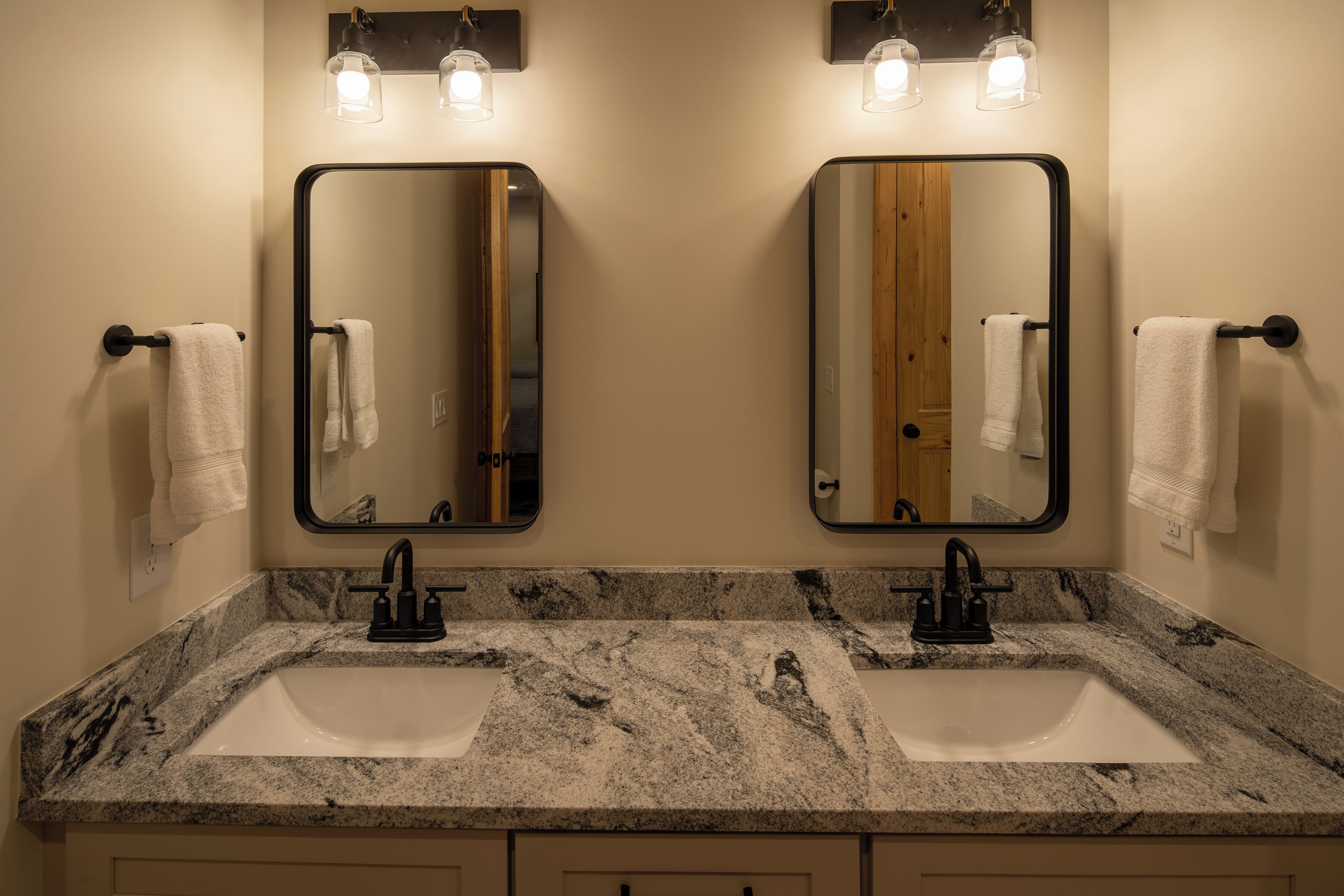 A bathroom with two sinks, a mirror, and wall-mounted lighting.