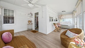 Un'ampia stanza con ventilatore a soffitto, mobili in vimini, un tavolo da pranzo con sedie e vista panoramica attraverso ampie finestre.