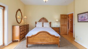 A bedroom with a wooden bed, a dresser, a nightstand, a mirror, and a door leading to another room. - Buena Vista (Fleetwood)