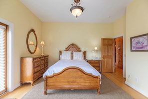 A bedroom with a wooden bed, a dresser, a nightstand, a mirror, and a door leading to another room. - Buena Vista (Fleetwood)