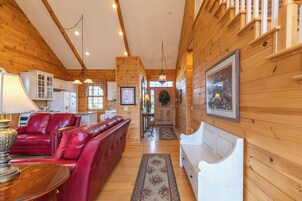 Interior de una cabaña de troncos con un sofá de cuero rojo, un banco blanco y armarios de madera.