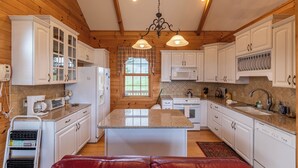 A kitchen with wooden walls, white cabinets, a central island, and a hanging light fixture. - Buena Vista (Fleetwood)