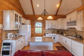 A kitchen with wooden walls, white cabinets, a central island, and a hanging light fixture. - Buena Vista (Fleetwood)