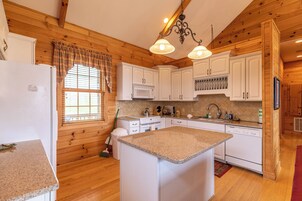 Una cocina con paredes de madera, armarios blancos, encimera de granito y una lámpara colgante.