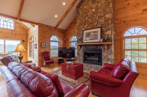 Un acogedor interior de cabaña de madera con chimenea de piedra, sofás de cuero y un televisor.