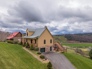 A large, yellow wooden house with a green roof, a stone garage door, and a wooden staircase leading to a porch. - Buena Vista (Fleetwood)
