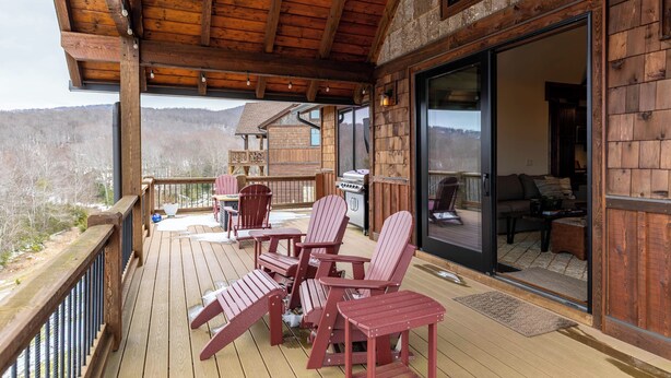 Eine Holzterrasse mit Adirondack-Stühlen, einem Grill und Blick auf die Berge.