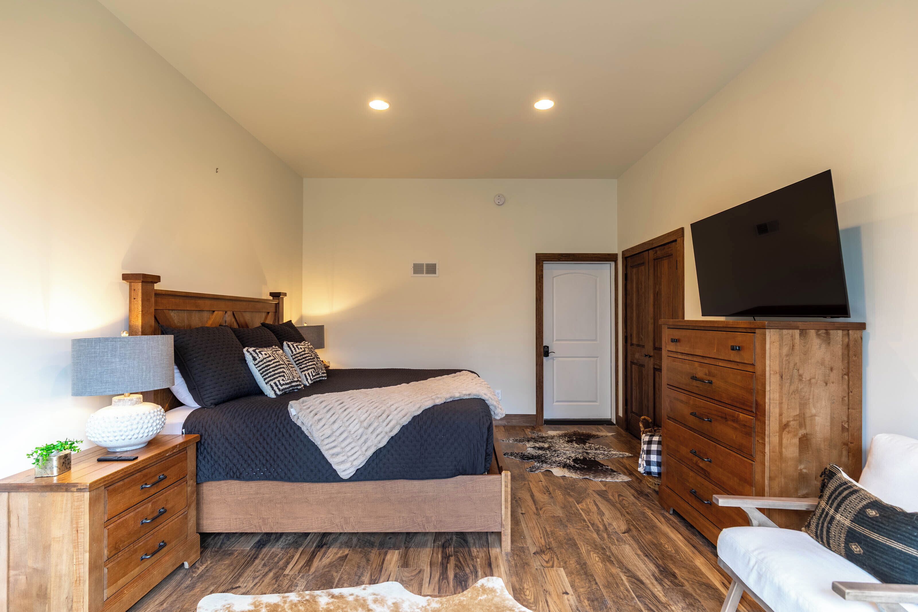 A bedroom with a bed, wooden dresser, TV, and a cowhide rug.