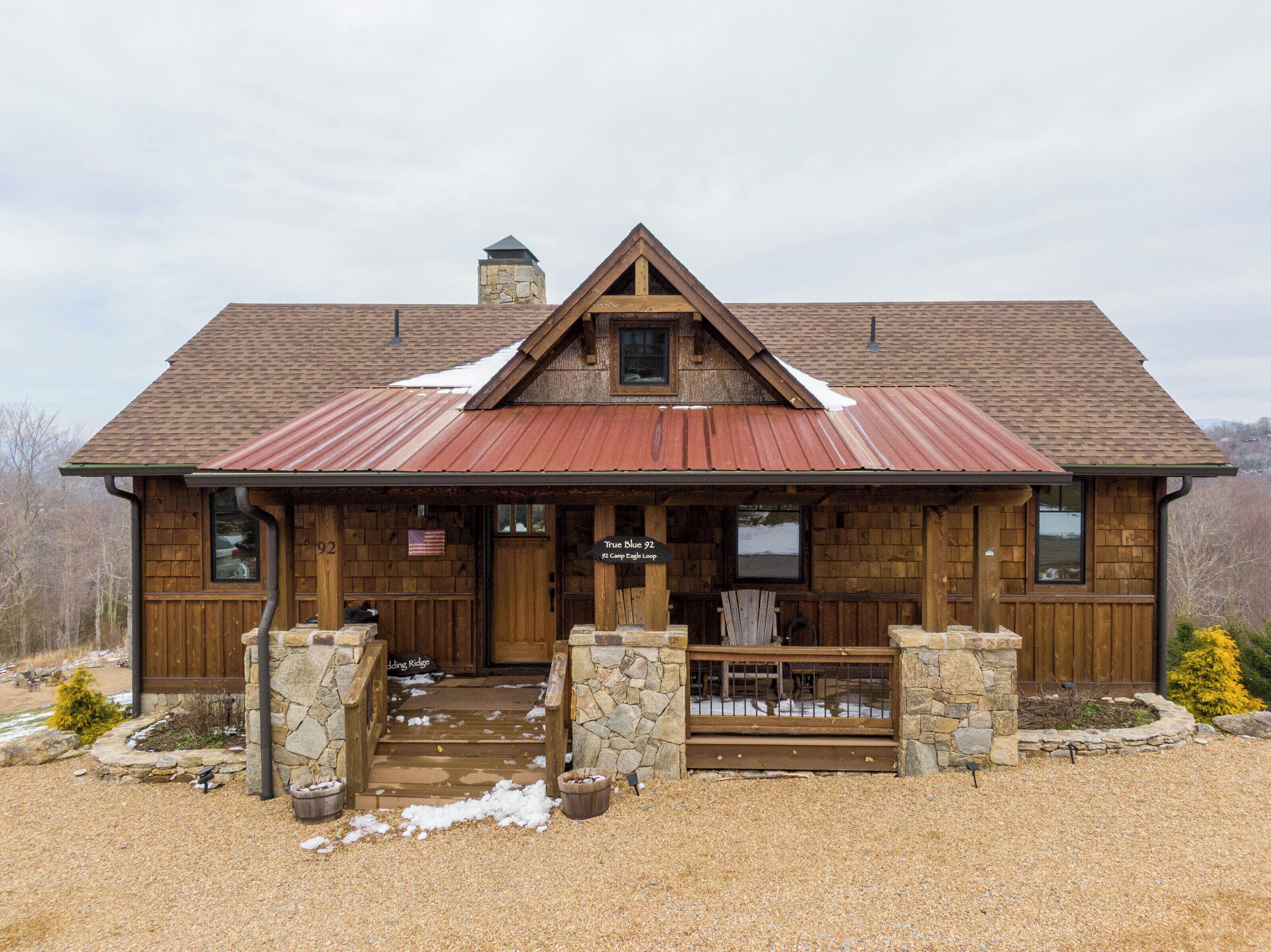 Un chalet rustique doté d’une cheminée en pierre, d’une façade en bois et d’un toit en métal.