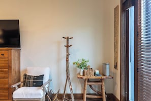 A room with a white chair, a wooden coat rack, a small table with a plant, a trash can, and a television on a wooden cabinet. - True Blue 92 at Eagles Nest (Banner Elk)