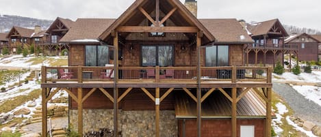 A large wooden lodge with a balcony, stone foundation, and multiple windows.