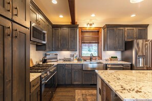 A kitchen with dark wooden cabinets, stainless steel appliances, a granite countertop, and a window with blinds. - True Blue 92 at Eagles Nest (Banner Elk)