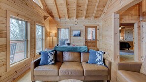 A cozy cabin interior with a leather sofa, wooden walls, and large windows. - High Time Cabin (Banner Elk)