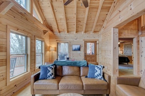 Ein gemütliches Blockhaus-Interieur mit einer Ledersofa, Holzwänden und großen Fenstern.
