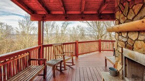 A wooden deck with a stone fireplace, benches, and a view of trees and mountains. - High Time Cabin (Banner Elk)