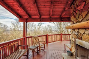Eine Holzterrasse mit einem Kamin aus Stein, Bänken und Blick auf Bäume und Berge.