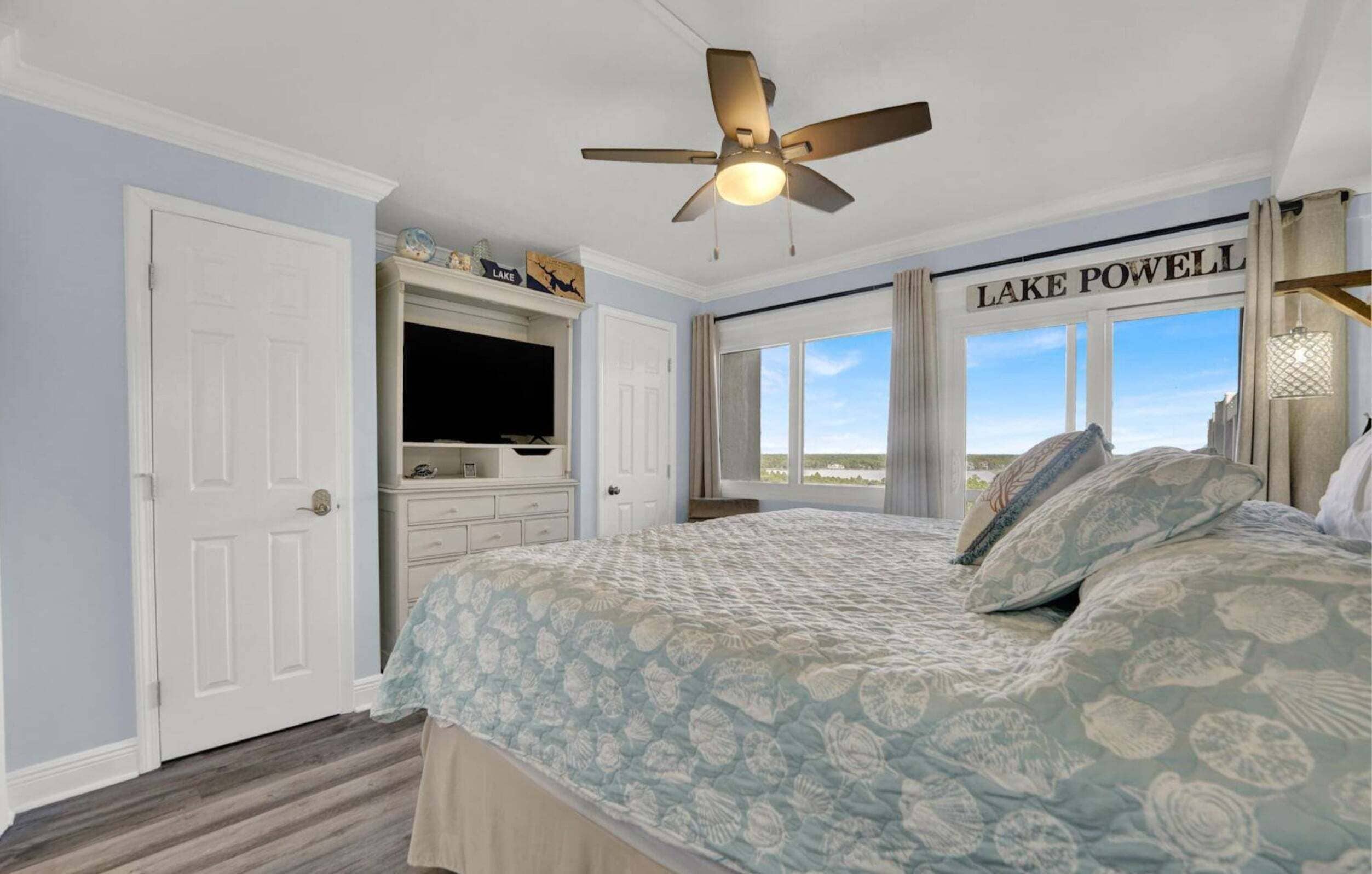 A bedroom with a bed, a ceiling fan, a television, a dresser, and a window with a view of the outdoors.