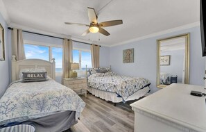 A bedroom with two beds, a ceiling fan, a window with curtains, a bedside table with a lamp, and a dresser. - Pinnacle Port Penthouse #29 (Panama City Beach)