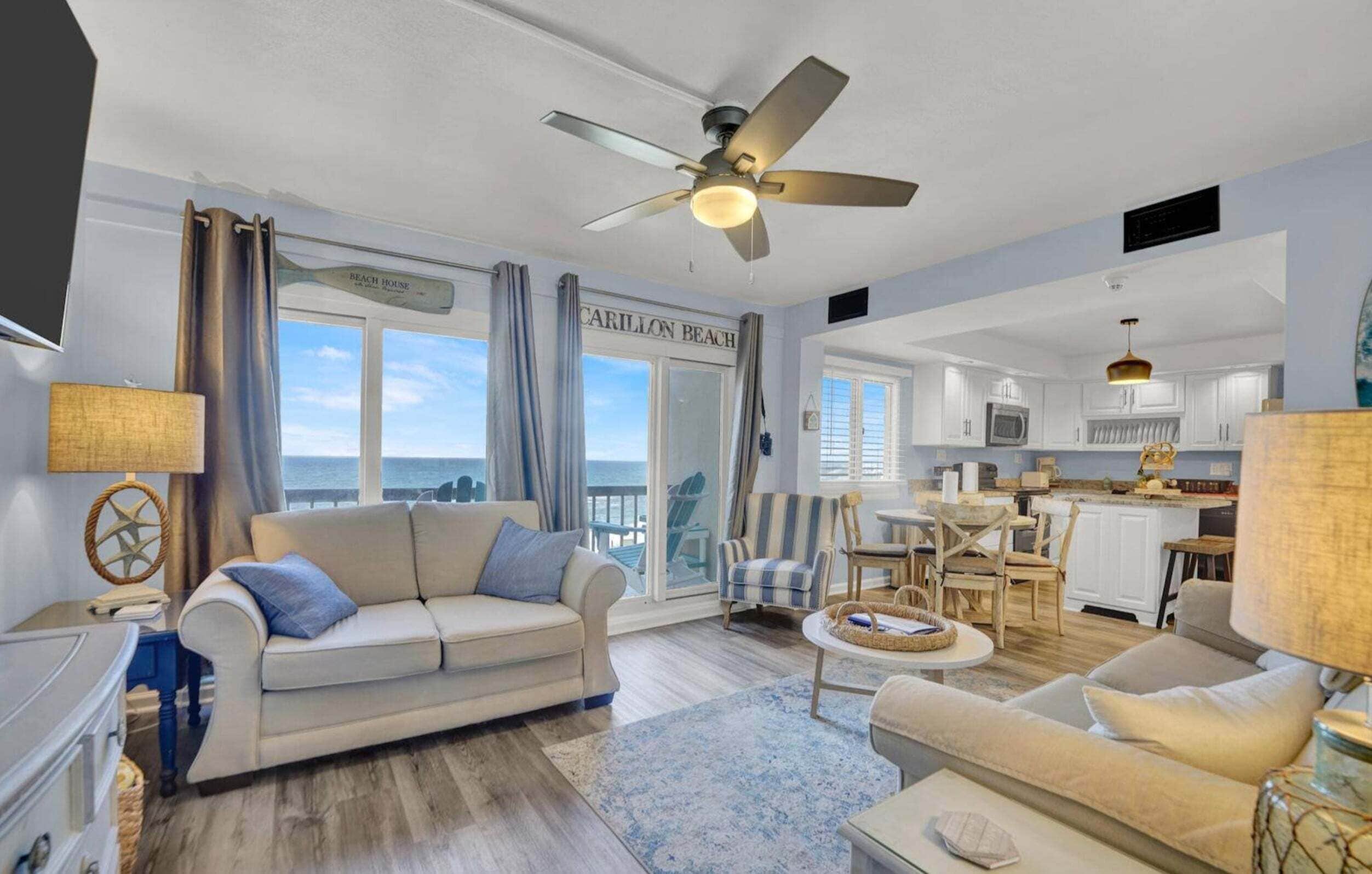 A spacious living room with a large window, a ceiling fan, and a view of the ocean.