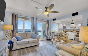 A spacious living room with a large window, a ceiling fan, and a view of the ocean.