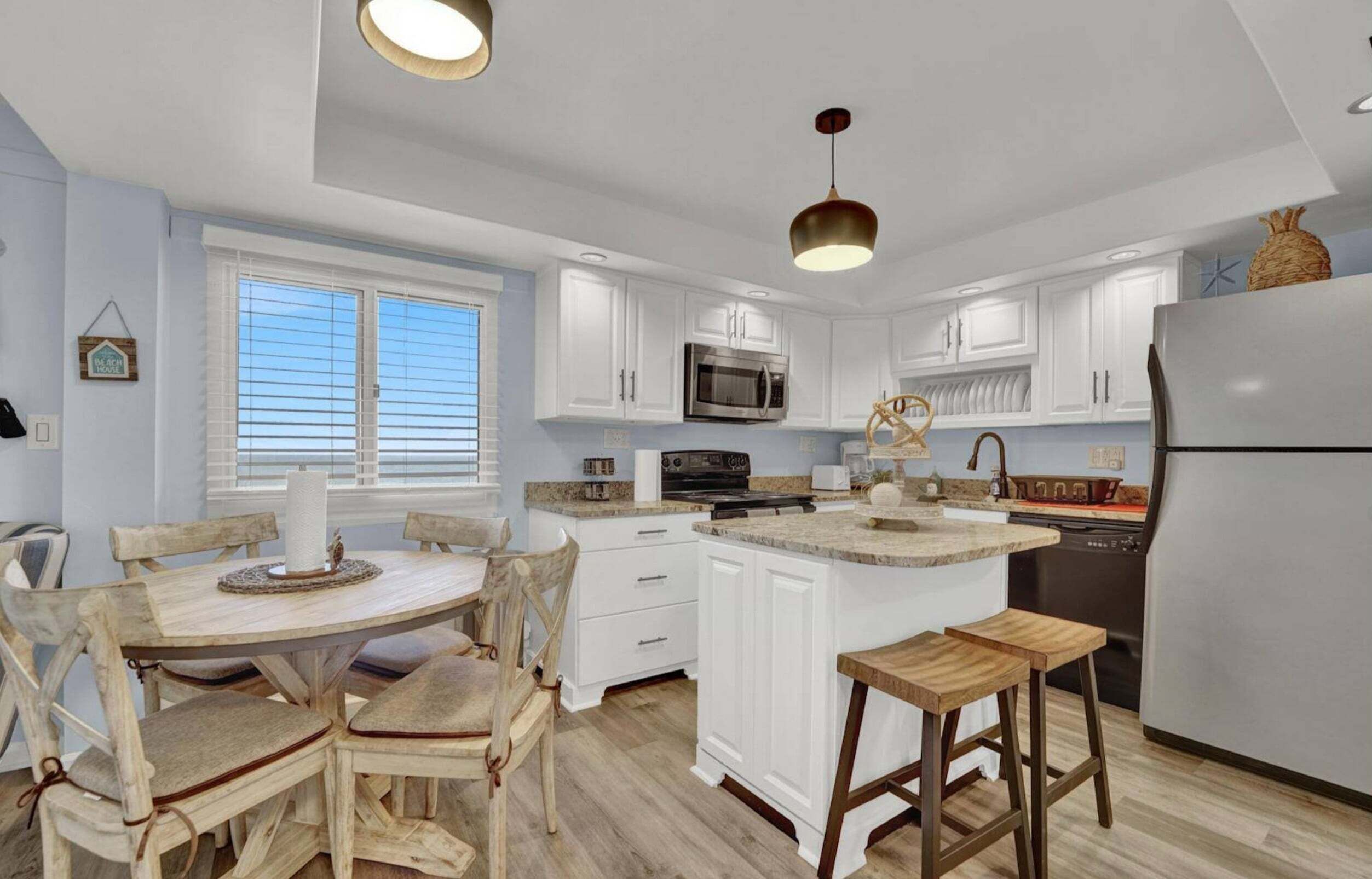 A kitchen with white cabinets, a central island, wooden chairs, and a hanging light fixture.