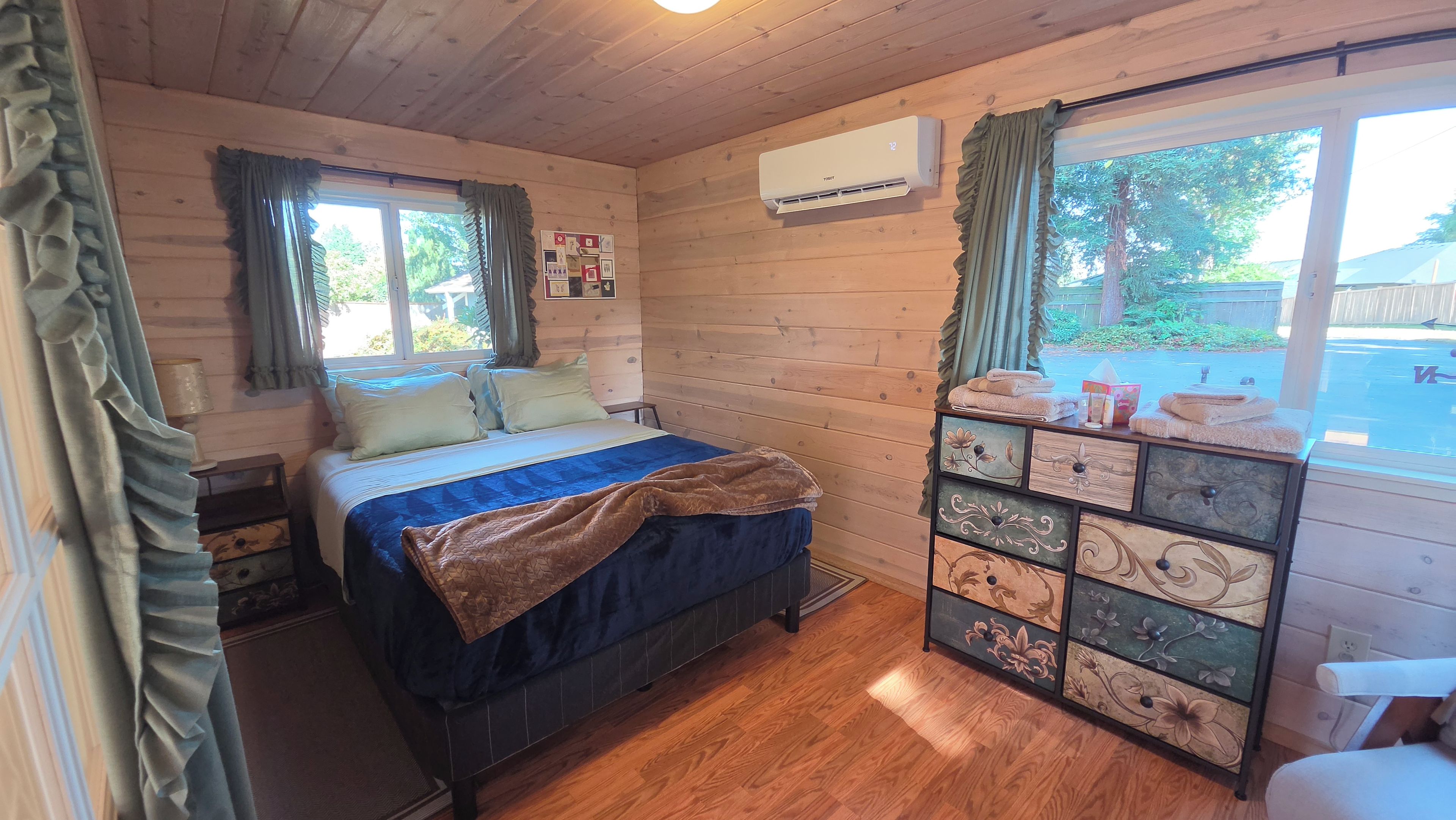 Une chambre dans un chalet en bois, comprenant un lit, une commode avec des tiroirs et un appareil de climatisation.