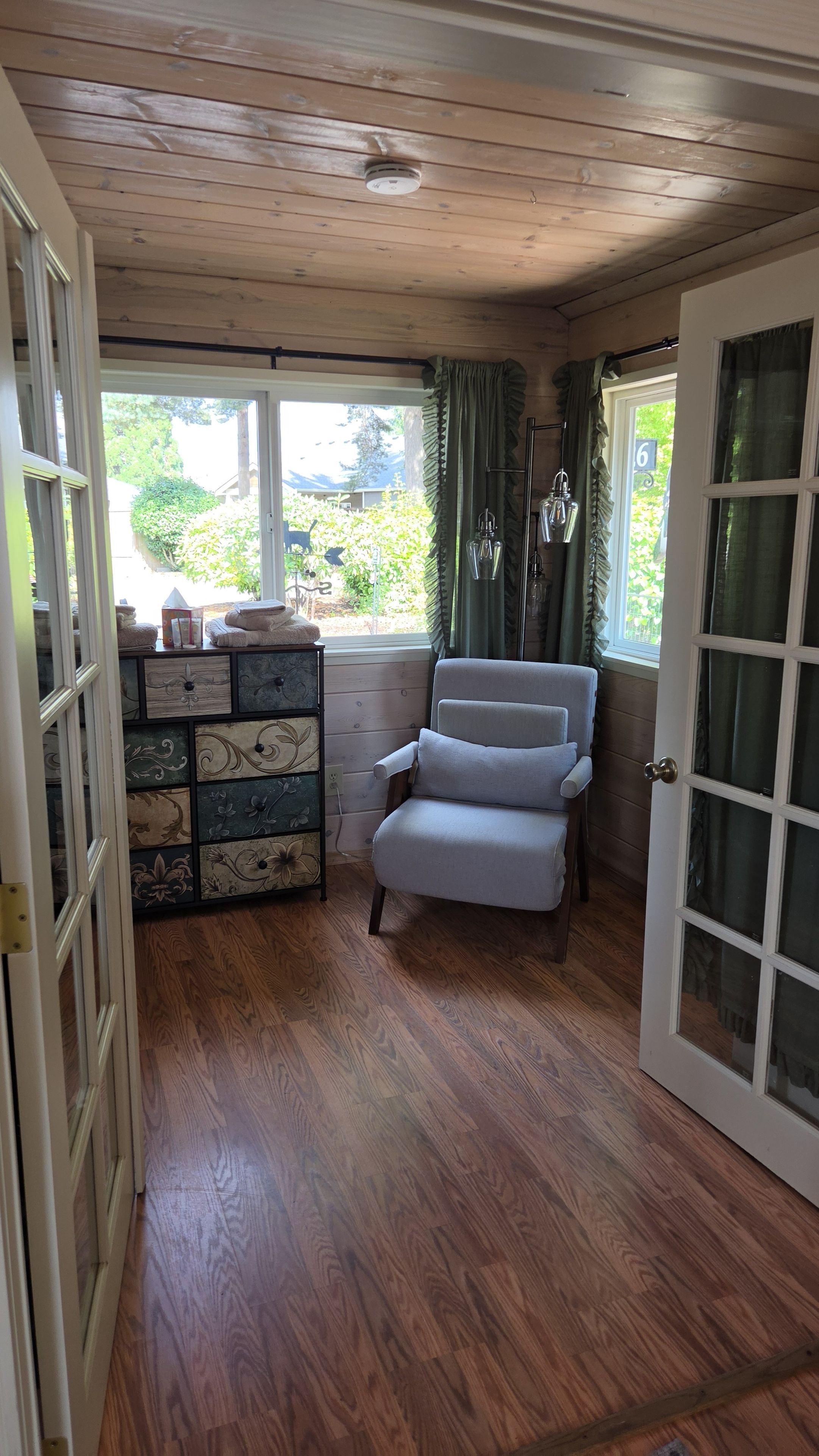 Une pièce avec un plafond en bois, un fauteuil rembourré, un plancher en bois et une fenêtre avec des rideaux.