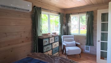 A room with wooden walls, a bed, a chair, a dresser, and a window with curtains.