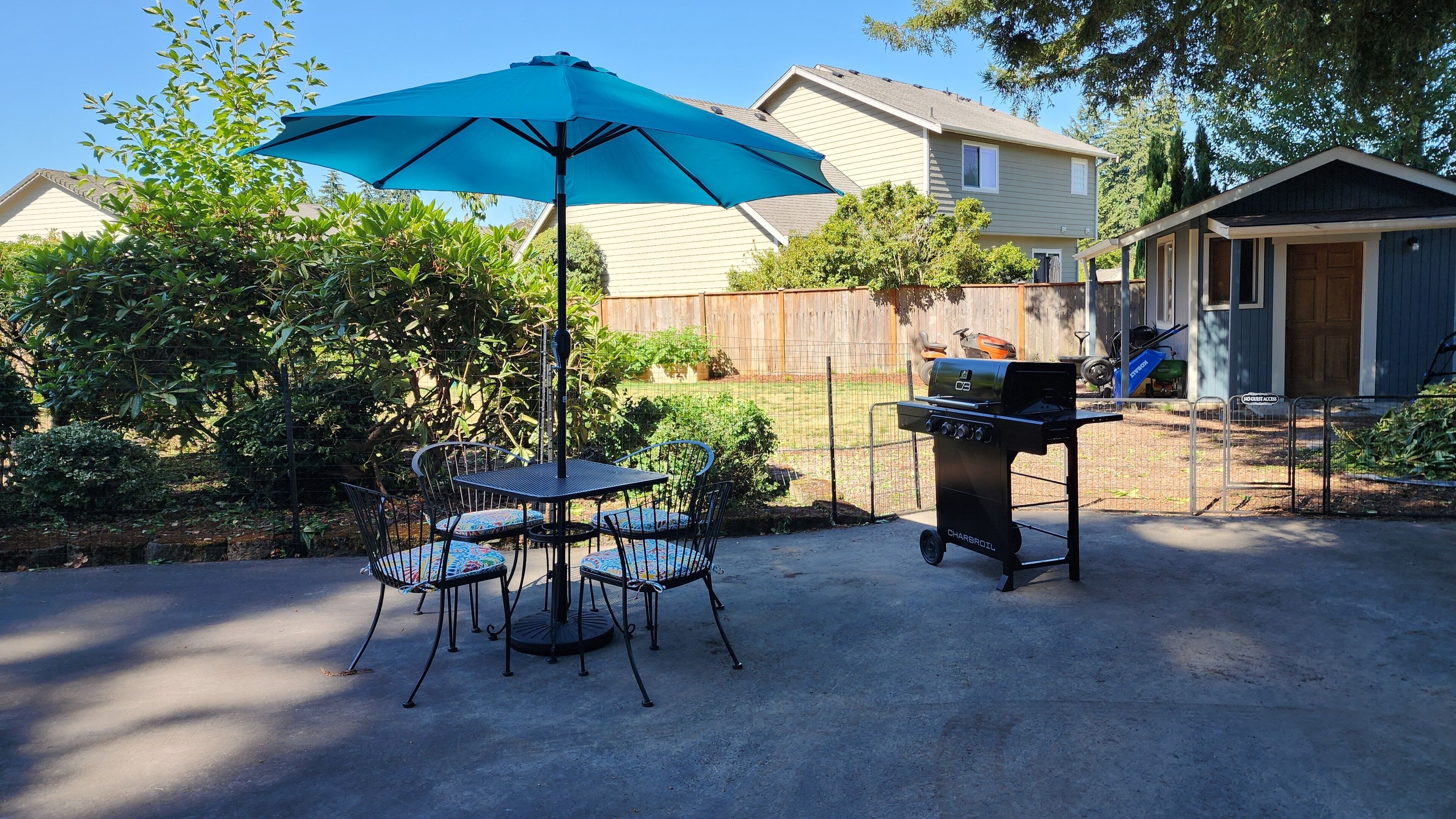 Een terras buiten met een tafel, stoelen, een barbecue en een blauwe parasol.