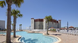A pool area with palm trees, lounge chairs, and a large hotel building in the background. - Laketown Wharf 1003 (Panama City Beach)