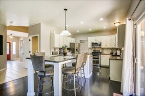 A modern kitchen with white cabinets, a central island with bar stools, stainless steel appliances, and a pendant light.