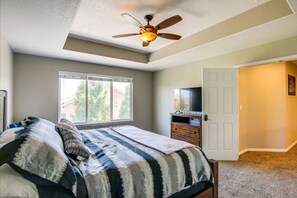 A bedroom with a bed, a ceiling fan, a window, a dresser, and a television.