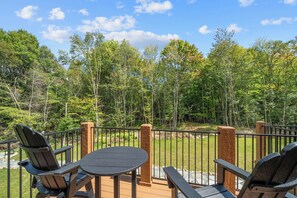 A deck with four Adirondack chairs and a round table, surrounded by a wooden railing, overlooking a forested area. - Creek Crossing at Eagles Nest (Banner Elk)