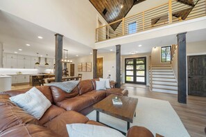 A spacious living area with a leather sofa, a coffee table, and a dining area with a kitchen in the background. - Creek Crossing at Eagles Nest (Banner Elk)